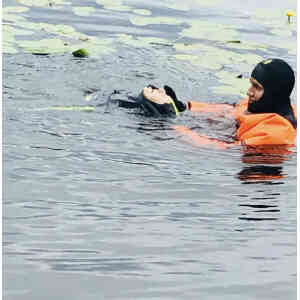 Person i orange dräkt räddar hund från vattnet.